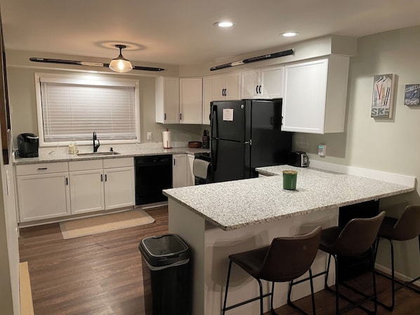 A kitchen with white cabinets, a black refrigerator, a coffee maker, and a trash can.