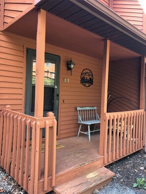 A wooden house with a porch, a bench, and a mountain logo on the wall.