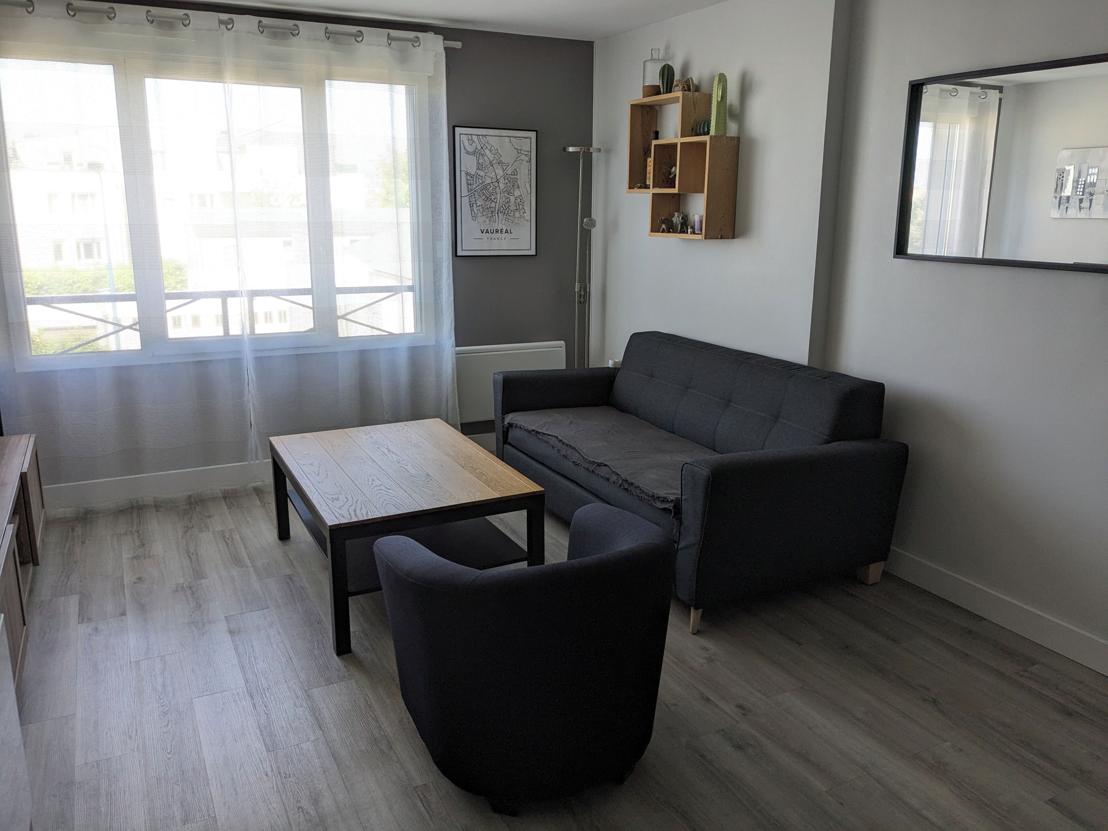A living room with a sofa, a coffee table, a chair, a map on the wall, and a window with curtains.