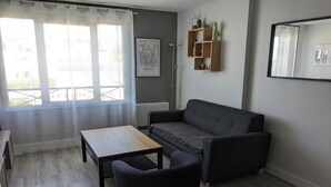 Ein Wohnzimmer mit Sofa, Couchtisch, Sessel, einer Karte an der Wand und einem Fenster mit Vorhängen.