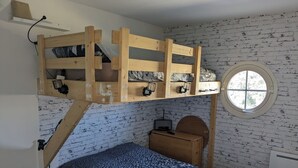 Ein Stockbett mit Schreibtisch und rundem Fenster in einem Zimmer mit Ziegelwand.