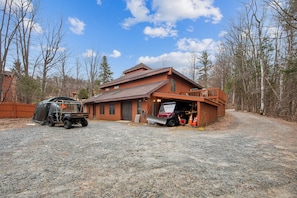 A large, rustic log cabin with a garage, a covered vehicle, and a gravel driveway.