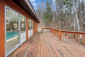 A wooden deck with glass doors leading to a pool, surrounded by trees.