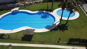 Une piscine à la forme originale, entourée d’une pelouse bien entretenue et de palmiers.