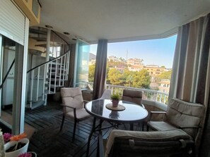 Un balcon avec une table et des chaises, un pot de fleurs et une vue sur des immeubles et des arbres.
