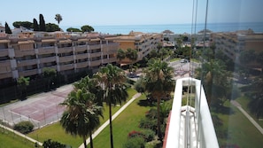 A residential area with multiple-story buildings, a tennis court, and a view of the sea.