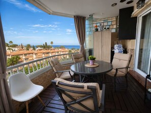 Un balcó amb una taula rodona i cadires, una planta en test i vista al mar i edificis.