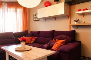 Uma sala de estar com um sofá roxo, uma mesa de centro de madeira e um vaso com flores.