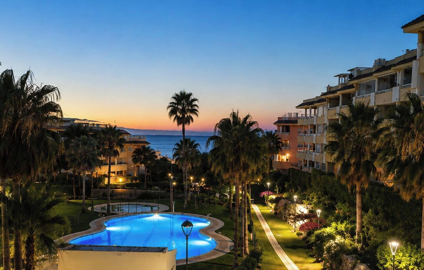 Een resort met een zwembad, palmbomen en uitzicht op de oceaan in de schemering.
