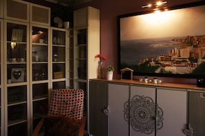 A room with a bookshelf, a chair, a cabinet with a decorative panel, and a large framed painting on the wall.
