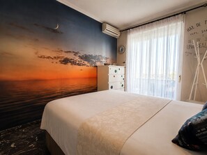 A hotel room with a large bed, a dresser, a wall-mounted air conditioner, and a view of the sea at sunset. - Duplex penthouse with pool, parking and magnificent sea and mountain views. (Fuengirola)