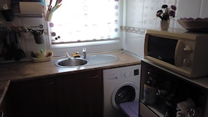 A kitchen with a sink, a microwave, a washing machine, and a window with a view.