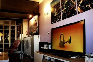 A living room with a large flat-screen TV, a bookshelf, a chair, and a window with a view of the city at night. - Duplex penthouse with pool, parking and magnificent sea and mountain views. (Fuengirola)