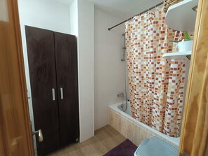 Une salle de bain avec un rideau de douche, une baignoire et une armoire en bois.