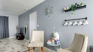 Ein Wohnzimmer mit grauer Wand, einer Uhr, einem Pflanzenregal und einer Wandleuchte.