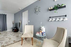Ein Wohnzimmer mit grauer Wand, einer Uhr, einem Pflanzenregal und einer Wandleuchte.