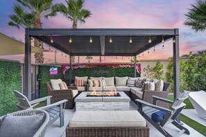 An outdoor patio with a covered seating area, a fire pit, and a decorative wall with flowers.
