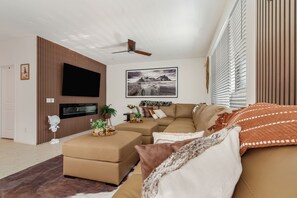 Un soggiorno con televisione a schermo piatto, ventilatore a soffitto, un grande quadro incorniciato e un divano marrone.