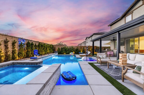 A backyard with a swimming pool, outdoor furniture, and a modern house.