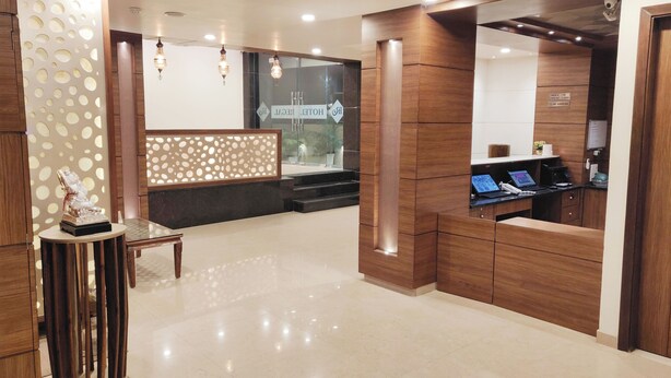 A hotel reception area with a wooden reception desk, a statue, and a glass partition with signage. - Hotel Regal (Amritsar)