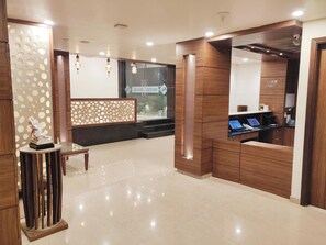 A hotel reception area with a wooden reception desk, a statue, and a glass partition with signage. - Hotel Regal (Amritsar)