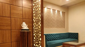 A room with a blue sofa, a glass coffee table, a wooden cabinet, and a decorative panel with circular cutouts. - Hotel Regal (Amritsar)