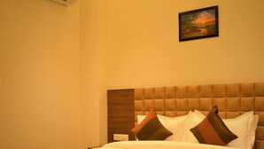A hotel room with a large bed, a headboard, a wall-mounted air conditioner, and a painting. - Hotel Regal (Amritsar)