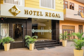 L’entrée d’un hôtel, avec une enseigne indiquant « HÔTEL REGAL », un logo composé des lettres « R » et « O », et un escalier menant à l’entrée.