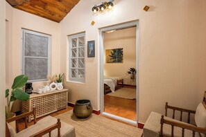 A cozy room with a wooden ceiling, a large window, a bedside table with a plant, and a bed with a white blanket.