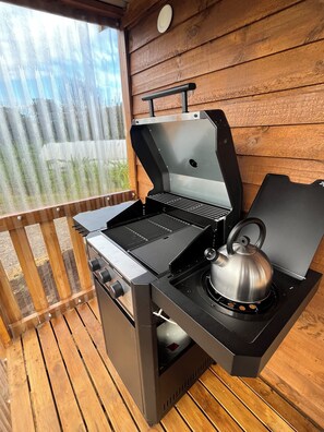A portable gas grill with a kettle on a wooden deck.