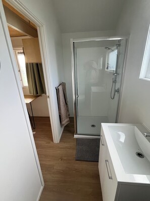 A modern bathroom with a glass shower enclosure, a white sink, and a towel rack.