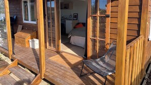 A wooden cabin with a deck, a bed, a kitchen, and a bathroom.