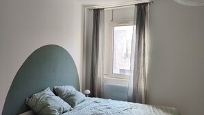 A bedroom with a bed, a round bedside table, a lamp, a window with curtains, and a radiator. - Lovely 2-bedroom apartment in Saint-Didier-en-Velay perfect for relaxing (Saint-Didier-en-Velay)