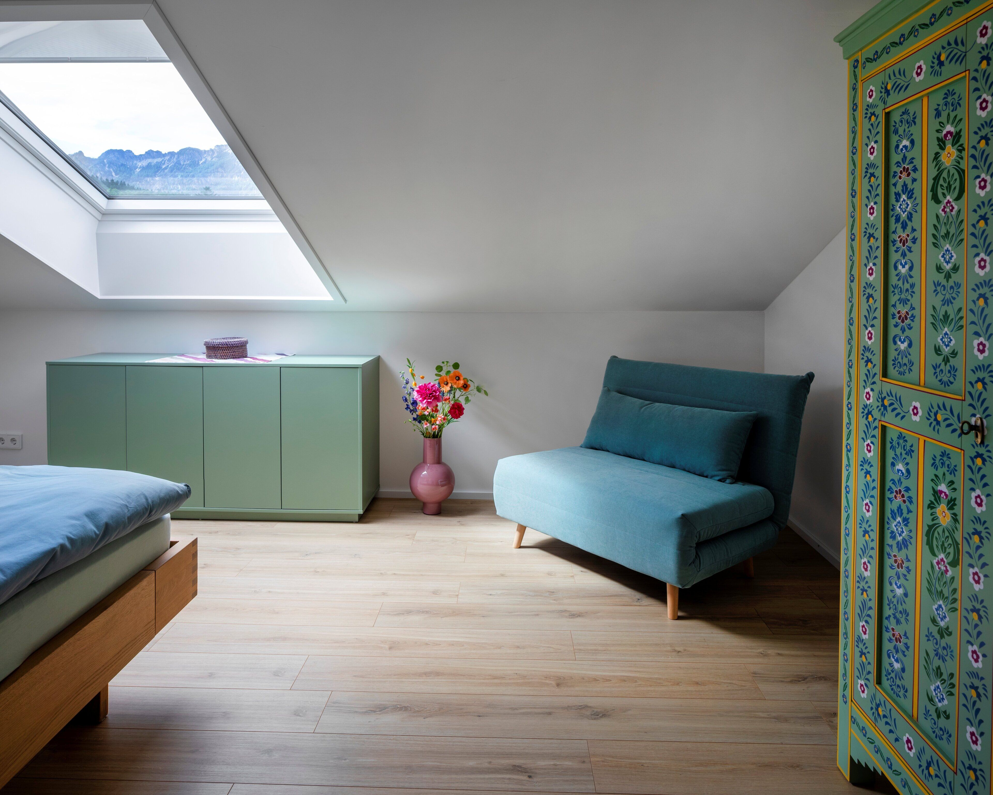 Ein Schlafzimmer mit Oberlicht, einem Bett, einer Couch, einem Schrank und einer Blumenvase.