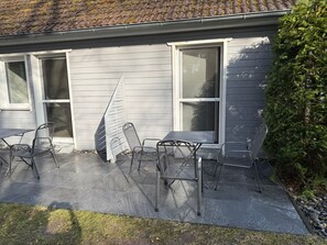 Een huis met een overdekte patio, metalen stoelen en een raam met hor.