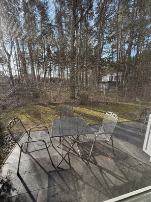Een omheind terras met een metalen tafel en stoelen, omgeven door bomen.