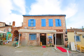 A brick building with blue shutters, a storefront, and a cobblestone street. - Blue Boz Ayvalık (Ayvalik)
