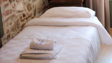 Un letto rifatto con un asciugamano piegato e un cuscino, una parete in mattoni e un comodino in legno.