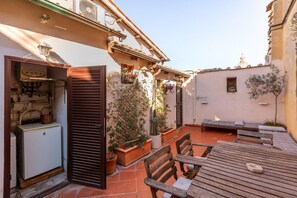 An outdoor patio with a table and chairs, potted plants, and a small building with a window and a door. - Farnese Wonderful Terrace (Roma)