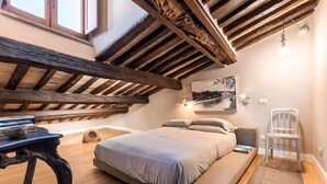 Ein Schlafzimmer mit schrägen Wänden, einem Bett, einem Sessel, einem Tisch und einer Wandleuchte.