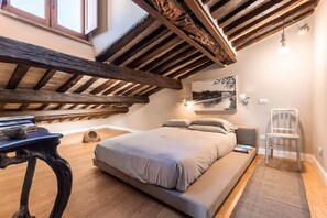 Ein Schlafzimmer mit schrägen Wänden, einem Bett, einem Sessel, einem Tisch und einer Wandleuchte.