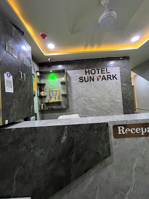 Zona de recepción de hotel con mostrador de mármol, un cartel que dice 'HOTEL SUN PARK' y un código QR en la pared.