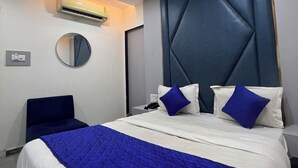 Moderni hotellihuone, jossa on suuri sänky, pyöreä peili, ilmastointilaite ja geometrisesti kuvioitu pääty.
