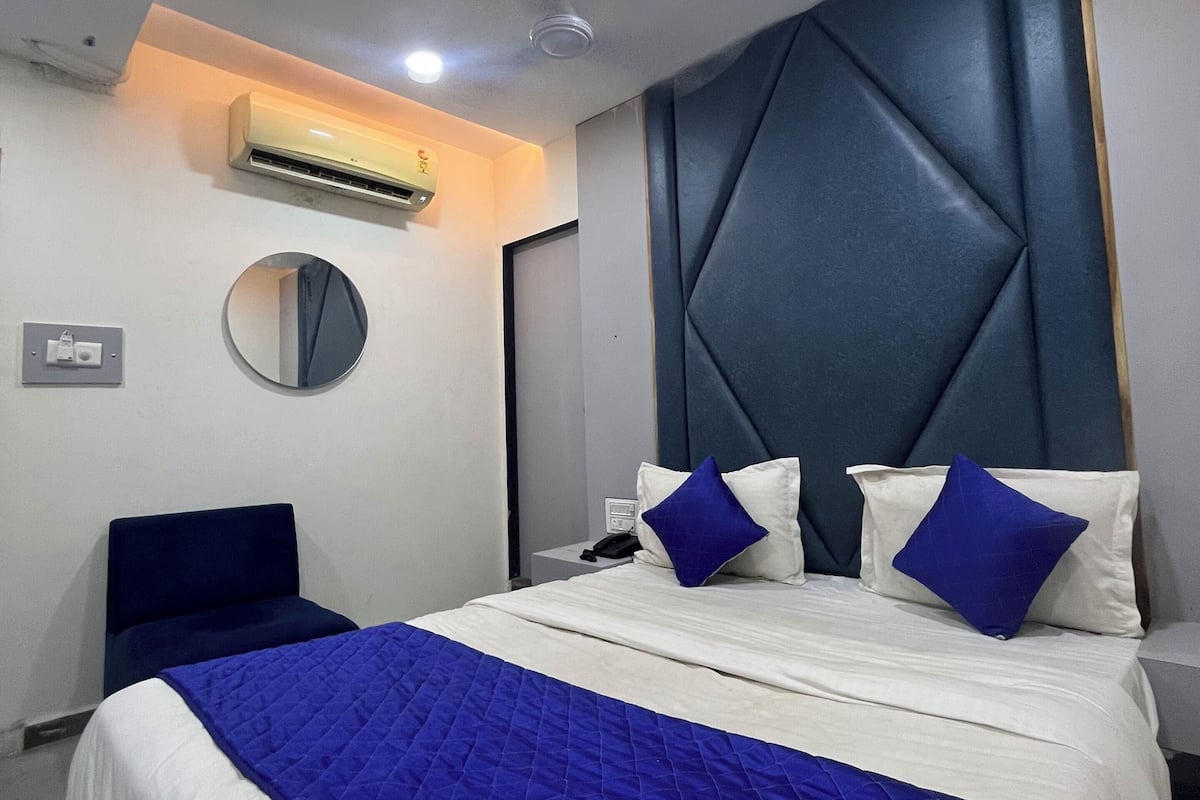 A modern hotel room with a large bed, a round mirror, an air conditioning unit, and a headboard with a geometric design.