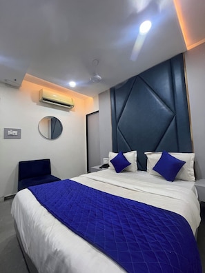 Una habitación de hotel moderna con una cama grande, un espejo redondo, un equipo de aire acondicionado y un cabecero con diseño geométrico.