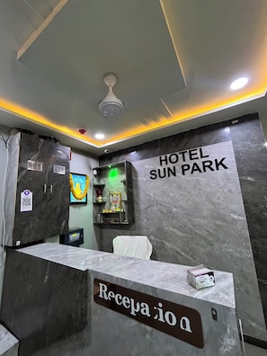 Vastaanottoalue, jossa on marmorinen palvelutiski, kattotuuletin ja seinälle kiinnitetty kyltti, jossa lukee: ”HOTEL SUN PARK”.