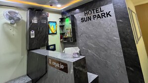 Vastaanottotiski, jossa on kyltti, jossa lukee ”Hotel Sun Park”, kattotuuletin, seinälle asennettu ilmastointilaite ja digitaalinen näyttö.
