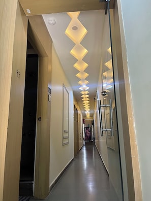 Pasillo de hotel con un diseño moderno en el techo, una puerta visible y un corredor que lleva a otra habitación.