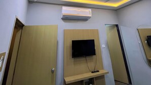 Hotellihuone, jossa on kattotuuletin, upotetut valaisimet, seinälle asennettu televisio ja sisäänrakennettu ilmastointilaite.