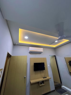 Habitación de hotel con ventilador de techo, iluminación empotrada, televisor montado y aire acondicionado integrado.